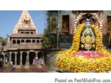 The image shows a Hindu temple with a large statue of a deity in the center. The statue is decorated with colorful flowers an...