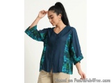 The image shows a young woman wearing a blue blouse with a green floral print. The blouse has a V-neckline and short sleeves...
