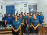 The image shows a group of people standing in an office. They are all wearing blue polo shirts with the logo of OM Solar Solu...