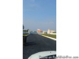The image shows a long, empty road with a blue sky in the background. The road appears to be in a residential area, as there...