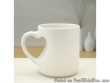 The image is of a white ceramic mug with a heart-shaped handle. The mug is sitting on a white surface with a blurred backgrou...