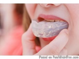 The image shows a close-up of a person's mouth, with their mouth slightly open. The person is holding a clear aligner in thei...