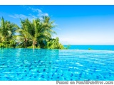 The image is a beautiful landscape of a swimming pool with crystal clear blue water. The pool is surrounded by lush greenery...