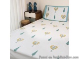 The image shows a bedroom with a bed in the center. The bed has a white comforter with a yellow and blue floral pattern on it...