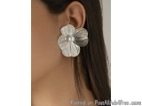 The image shows a close-up of a person's ear. The earring is in the shape of a flower with a pearl in the center. The flower...