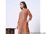 The image shows a young woman wearing a traditional Indian outfit. She is standing in front of a wooden cabinet with intricat...