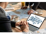 The image shows a group of people sitting around a table with a laptop in the center. The laptop screen displays the word "SE...