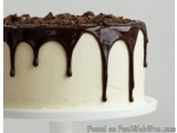 The image is of a cake on a white cake stand. The cake is a two-tiered cake with a white base and a creamy white frosting. On...