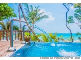 The image shows a beautiful tropical resort with a swimming pool in the foreground. The pool is surrounded by palm trees and...