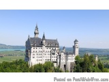 The image is a panoramic view of a large castle with multiple towers and turrets on top of a hill. The castle is located in a...