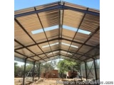 The image shows the interior of a large metal structure with a curved roof. The roof is made up of wooden slats arranged in a...
