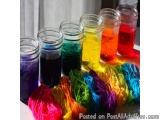 The image shows six small glass jars filled with different colored liquids. The jars are arranged in a row on a white surface...