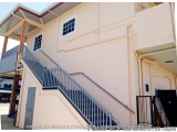 The image shows the exterior of a two-story building with a beige exterior and a black metal staircase. The staircase has a m...