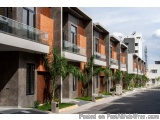 The image shows a row of modern apartment buildings with a street in front of them. The buildings are made of concrete and br...