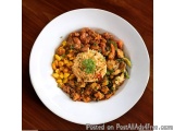 The image shows a plate of food on a wooden table. The plate is white and round, and it is filled with a colorful dish. The d...