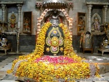 The image shows a Hindu temple decorated with flowers and garlands. In the center of the image, there is a large statue of a...