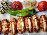 The image shows a plate of grilled chicken skewers. The skewers are arranged in a circular pattern on a white plate. The chic...