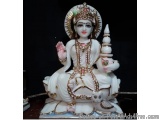 The image is a photograph of a statue of the Hindu goddess Lakshmi. She is sitting on a lotus flower with her legs crossed an...