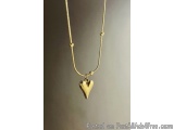 The image is of a gold necklace with a pendant in the shape of a heart. The necklace is made of a thin gold chain with small...