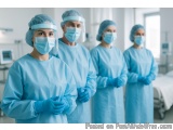 The image shows a group of four medical professionals standing in a hospital room. They are all wearing blue surgical gowns,...
