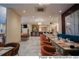The image shows the interior of a modern restaurant with a high ceiling and white walls. The floor is made of marble tiles an...