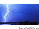 The image shows a lightning bolt striking over a body of water. The sky is a deep blue color and the lightning bolt is bright...