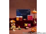 The image shows a collection of Indian sweets and offerings on a red cloth-covered table. On the left side of the table, ther...