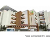 The image is a 3D rendering of a modern hotel building. The building is white with a brown and orange facade. The entrance of...
