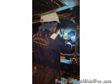 The image shows a man wearing a hard hat and a blue coverall with a yellow logo on it. He is standing in front of a large mac...
