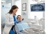 The image shows a dentist and a patient in a dental clinic. The dentist is wearing a white coat and blue gloves and is standi...
