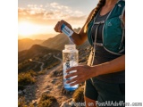 The image shows a young woman standing on a mountain trail with a backpack on her back. She is holding a blue water bottle wi...