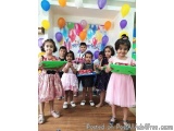 The image shows a group of young children standing in front of a birthday banner that reads "Happy Birthday". The children ar...