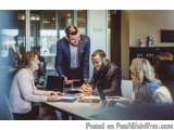 The image shows a group of people in a meeting room. There are four people in the image, three men and two women, sitting aro...