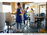 The image shows a group of three people in an office setting. They are all wearing blue aprons and yellow rubber gloves and a...