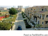 The image shows a residential area with a row of multi-storey houses on the right side. The houses are painted in a light bei...