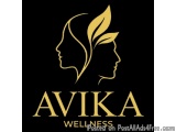The image is a logo for Avika Wellness. It is a black background with a gold-colored logo in the center. The logo features tw...
