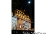 The image shows the entrance of a store at night. The store is located on a street corner and is lit up with bright lights. T...