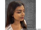 The image is a close-up portrait of a young woman with long dark hair. She is wearing a white t-shirt and a gold necklace. He...