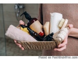 The image shows a person holding a basket filled with various bathroom items. The basket is made of woven straw and is held i...