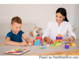 The image shows a mother and son playing with colorful building blocks on a wooden table. The mother is sitting at the table...