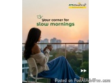 The image shows a young woman sitting on a balcony with a view of a city skyline. She is wearing a long blue dress and a whit...