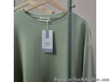 The image shows a green long-sleeved t-shirt hanging on a wooden hanger. The shirt has a round neckline and appears to be mad...
