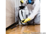 The image shows a person wearing a white protective suit and a blue gas mask, kneeling on the floor and using a pressure wash...