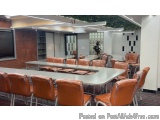The image shows a large conference room with a long table in the center. The table is made of metal and has a rectangular sha...