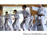 The image shows a group of young boys in a martial arts class. They are wearing white karate uniforms with black belts and ar...