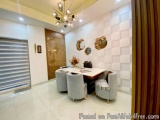 The image shows a modern and luxurious dining area in a modern home. The room has a high ceiling with a large chandelier hang...