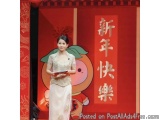 The image shows a young woman standing on a stage in front of a red background with Chinese characters written in white. She...