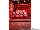 The image shows a home theater with red leather seats. The walls are painted in a deep red color and there is a projector scr...