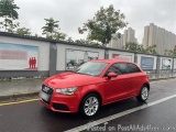 The image shows a red Audi car parked on the side of a road. The car is a hatchback model with a sleek design and silver allo...