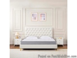 The image shows a modern bedroom with a large white bed in the center. The bed has a tufted headboard with a buttoned design...